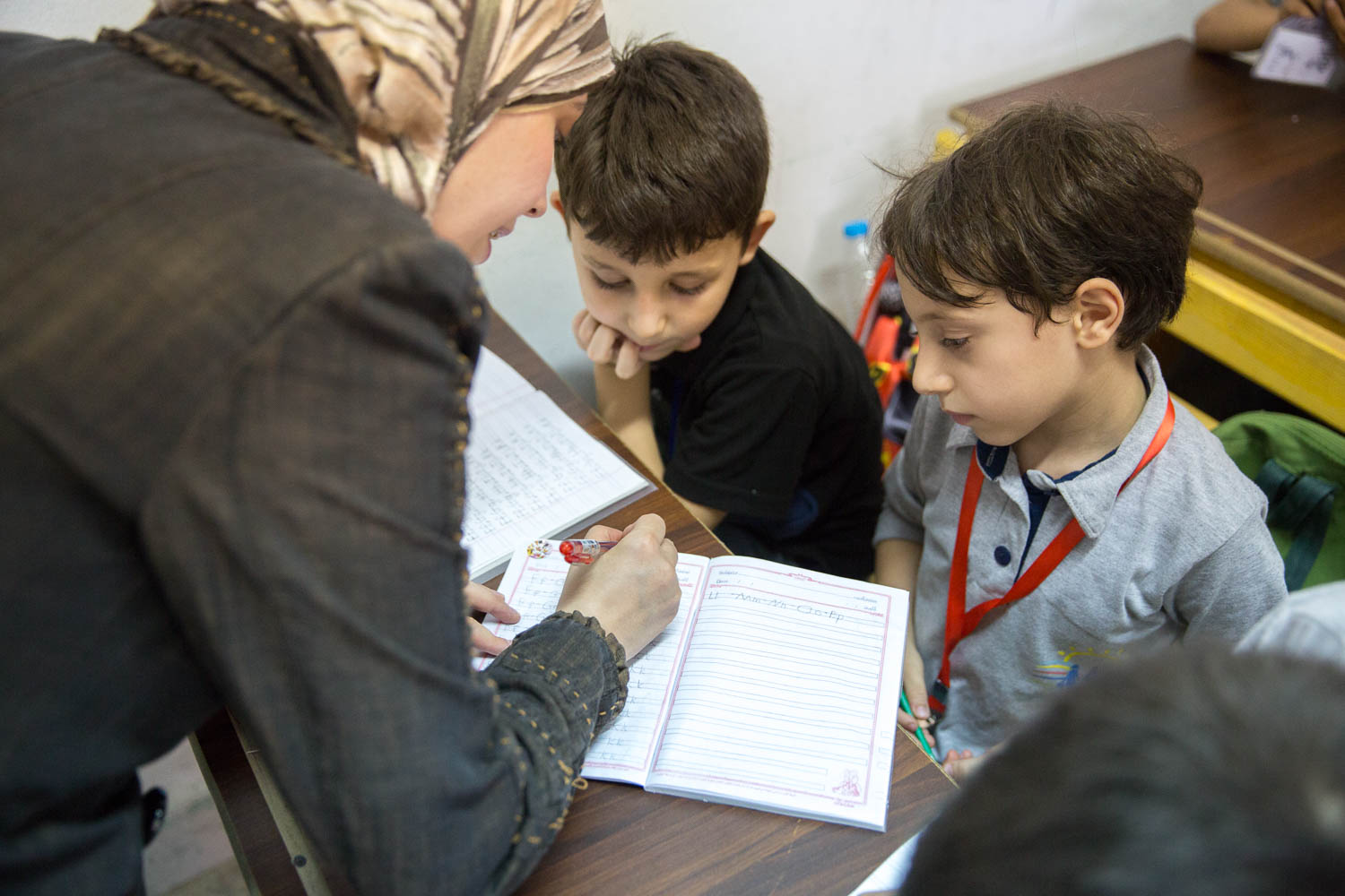  A teacher helps children write the alphabet during one of their first English lessons at the community centre run by NGO Ansan and Plan International. Most of the teachers at the community centre are Syrian refugees themselves. 