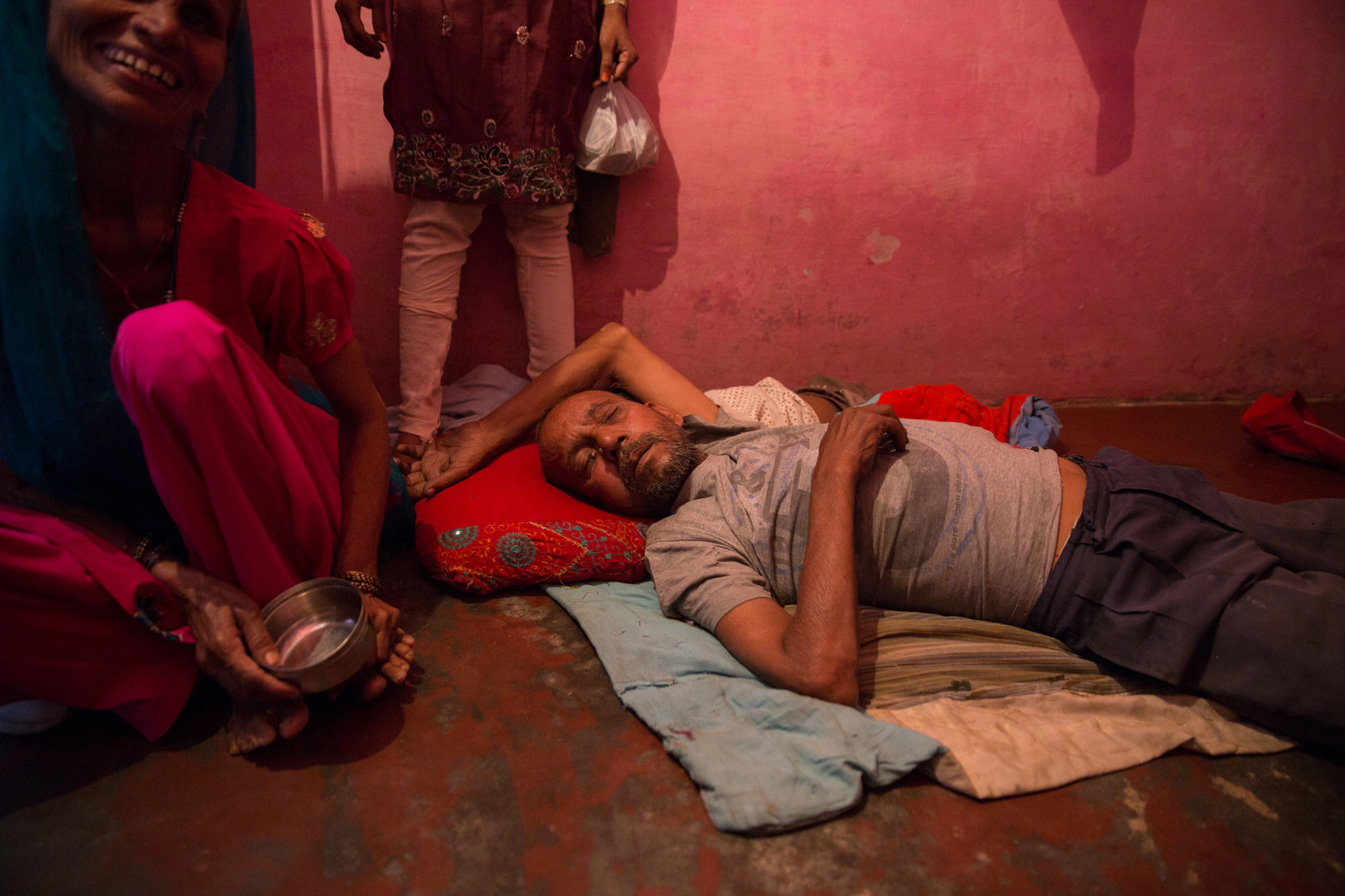  A man sleeps off his hangover in the middle of the afternoon, surrounded by his wife and children. Alcoholism is a common problem in the neighborhood. 